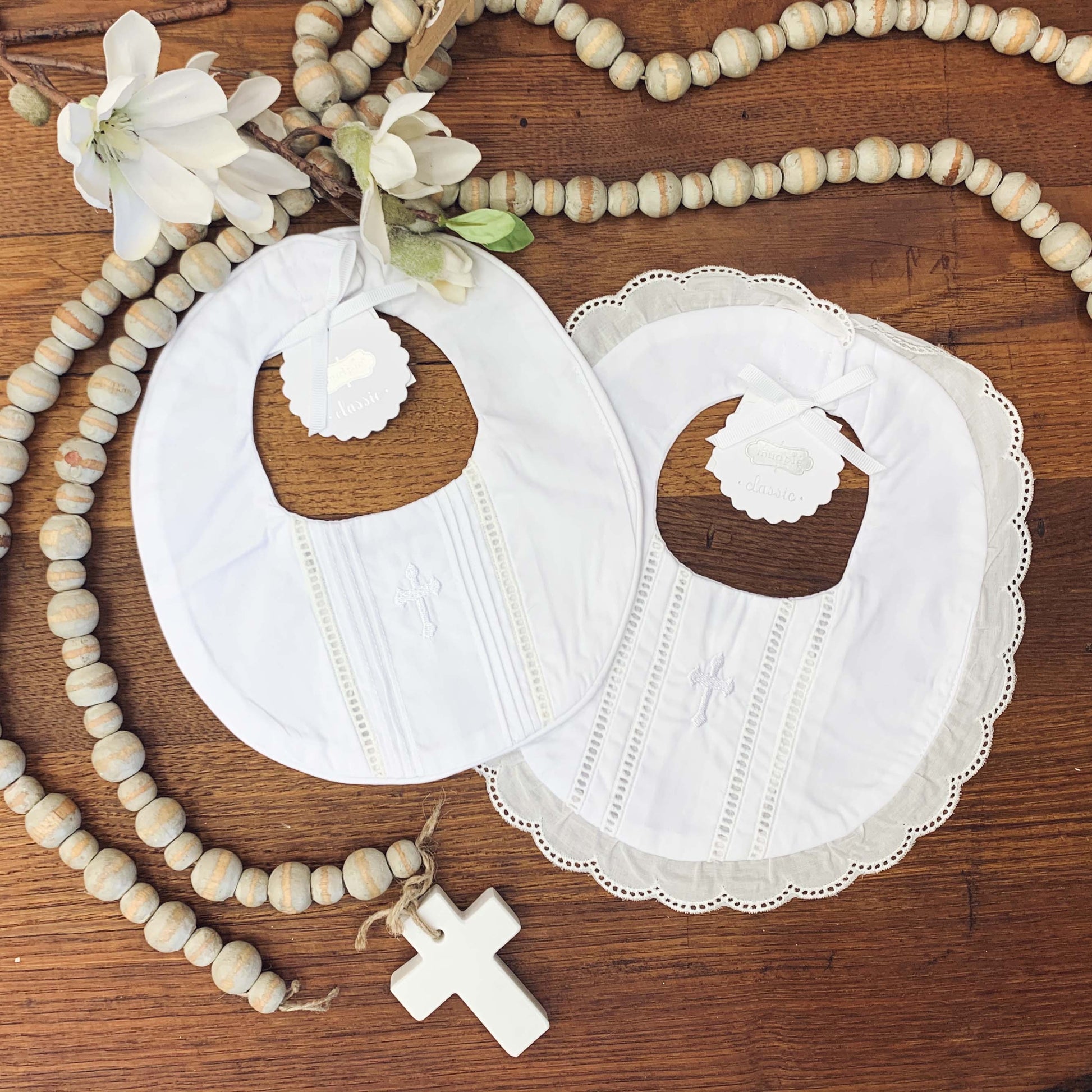 wooden bead cross alongside scalloped and unscalloped white christening bibs